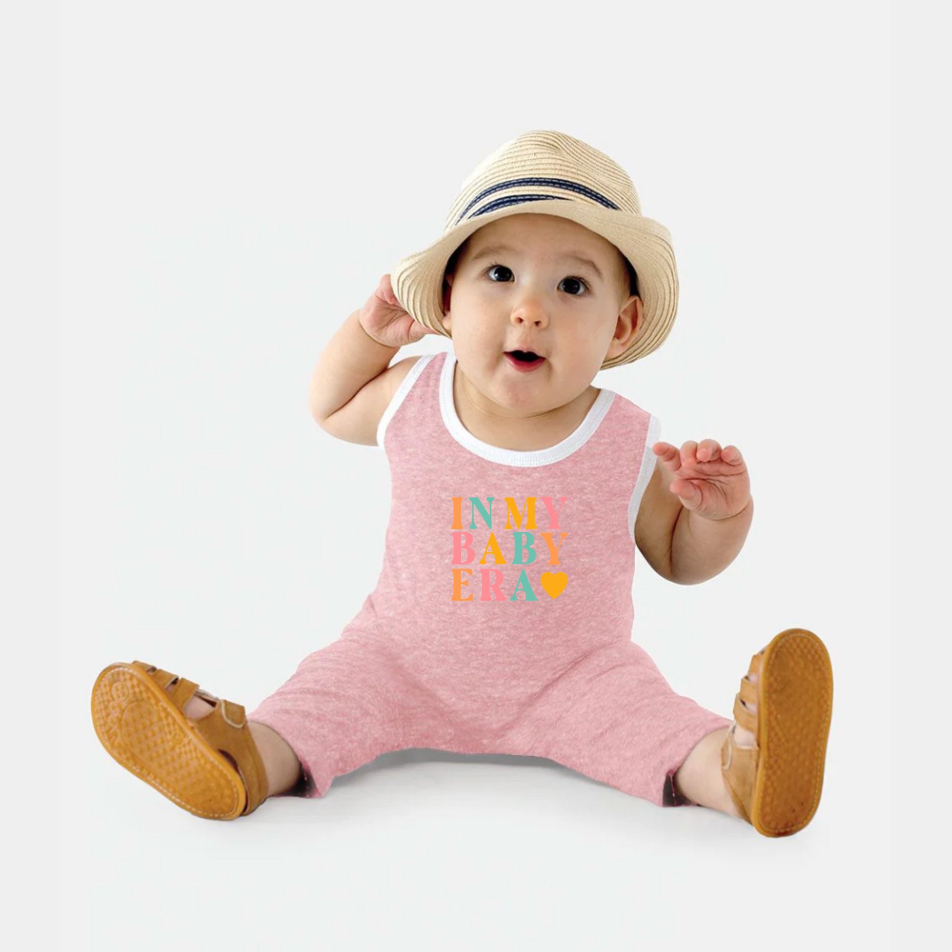 Baby wearing a pink romper with colorful text and a straw hat on a white background