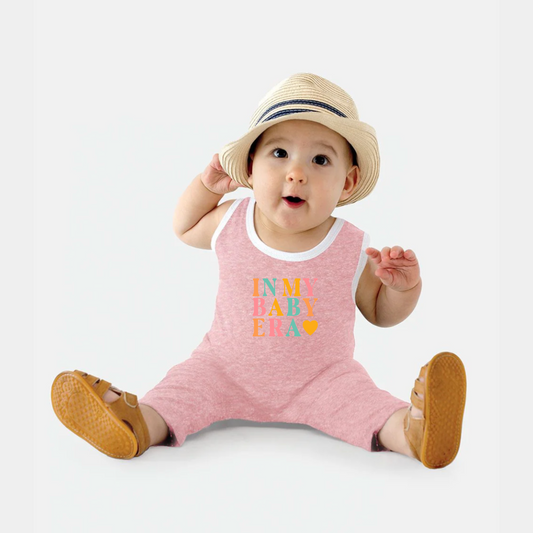 Baby wearing a pink romper with colorful text and a straw hat on a white background