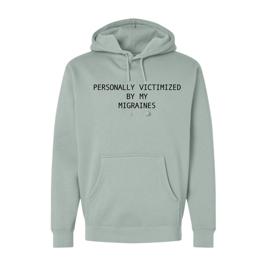 Light green hoodie with text 'PERSONALLY VICTIMIZED BY MY MIGRAINES' on a white background