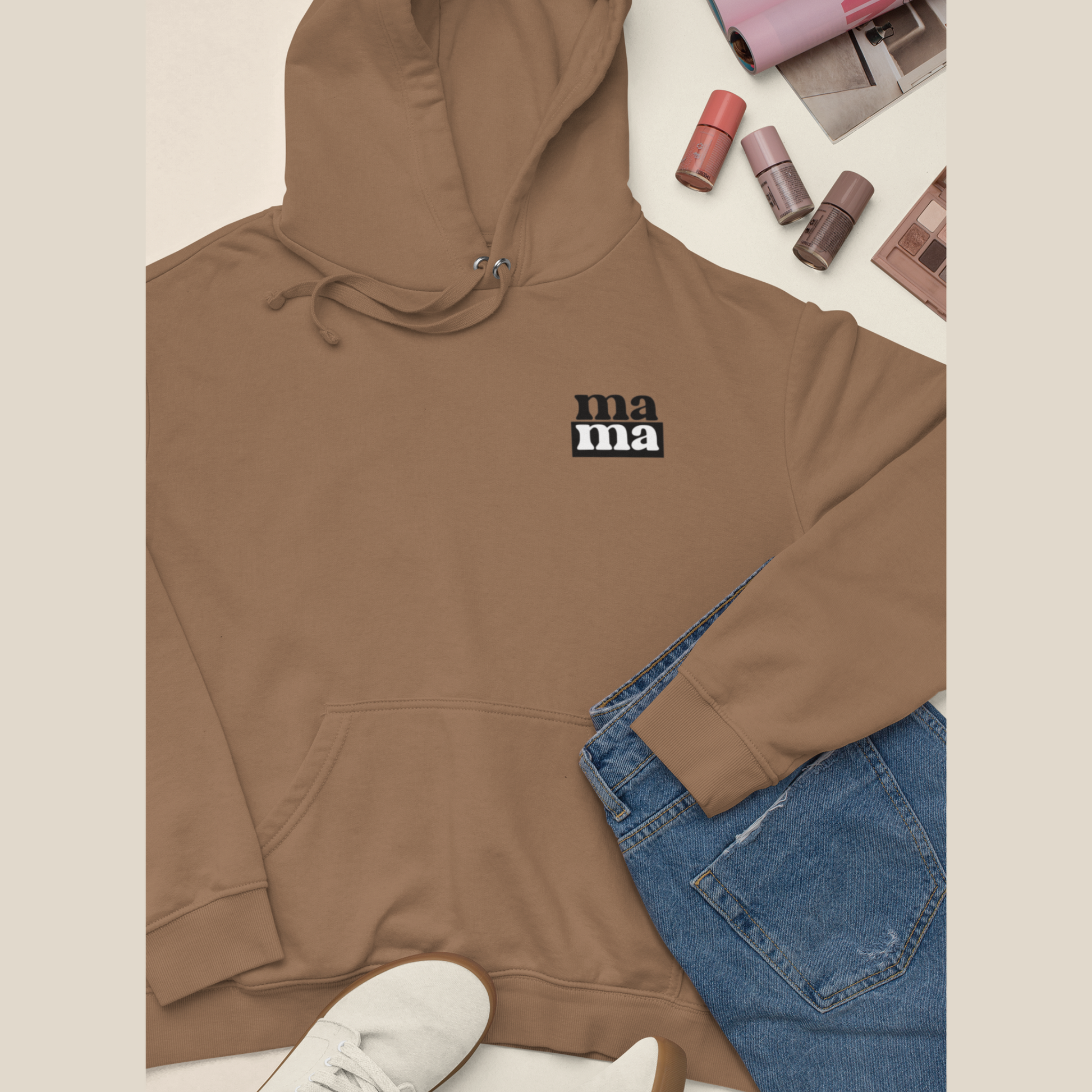 Brown hoodie with 'ma ma' text, blue jeans, and shoes on a beige background