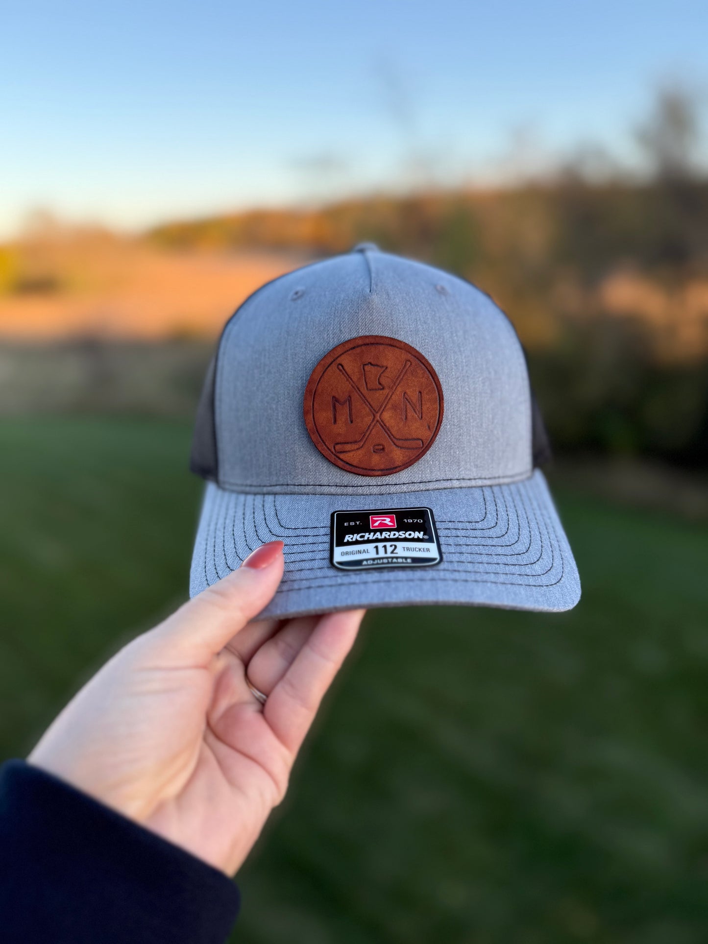 Gray cap with leather patch held by a hand against a blurred natural background