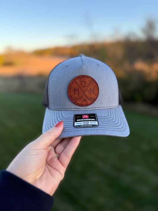 Gray cap with leather patch held by a hand against a blurred natural background