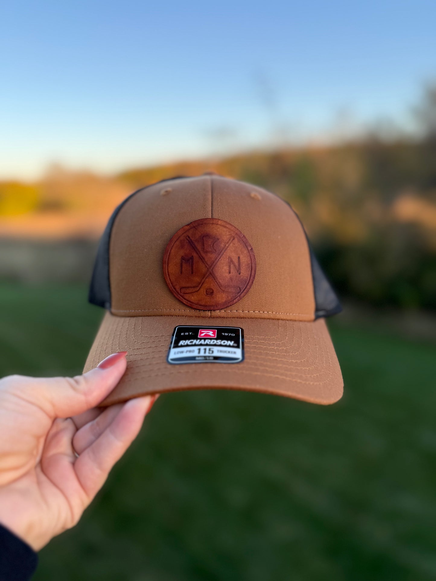Brown cap with leather patch held in front of a blurred natural background