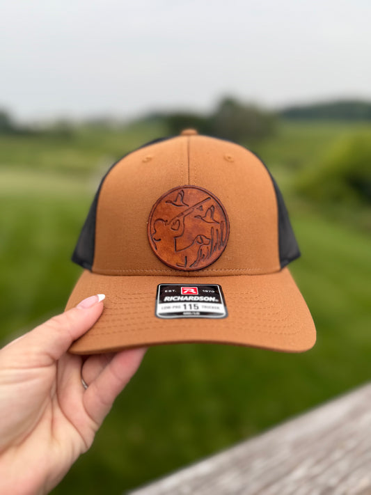 Brown and black cap held by a hand with a blurred green field background