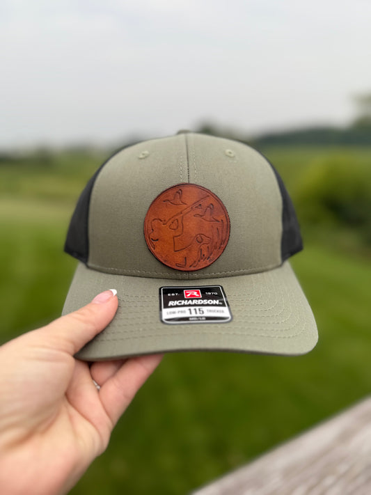Green cap with leather patch held by a hand against a blurred green background
