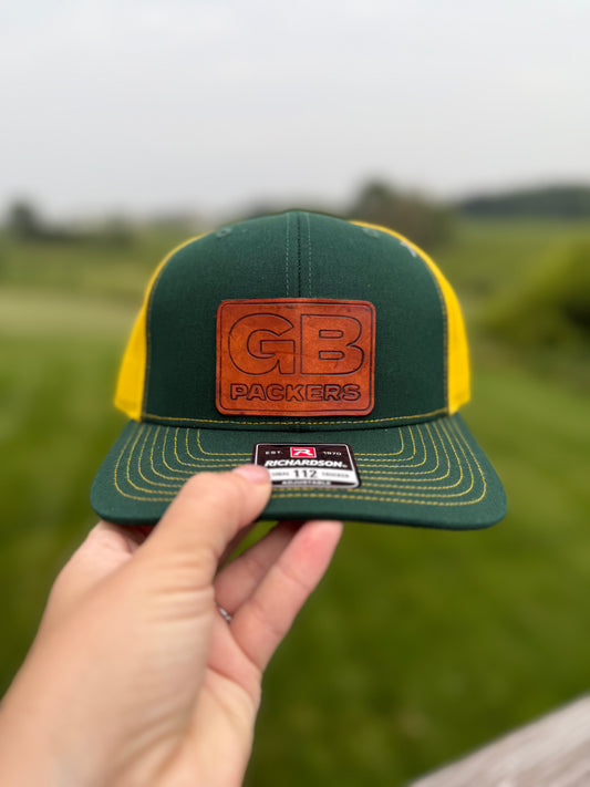 Green and yellow cap with a leather patch held in front of a blurred green field.