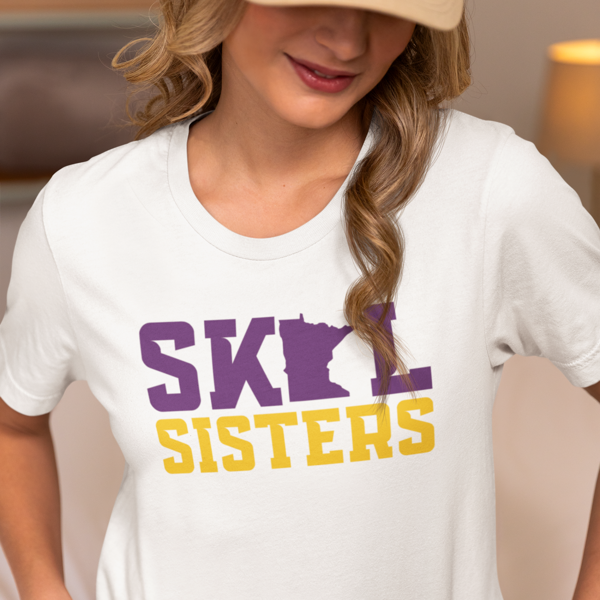 Person wearing a white t-shirt with 'SKOL SISTERS' printed in purple and yellow.