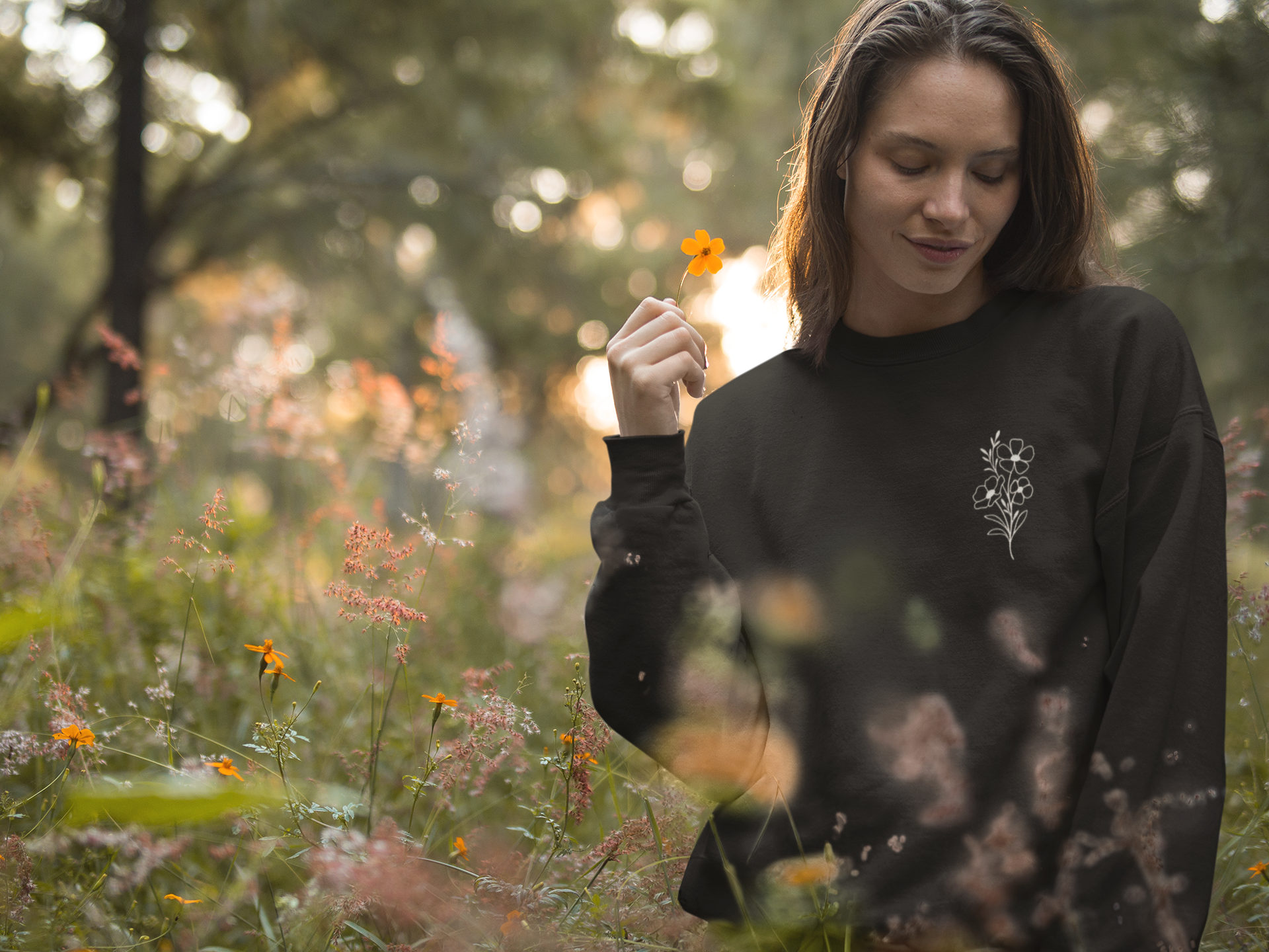 Front view of the sweatshirt on a model in a field of flowers. Black sweatshirt has a flower design on it.