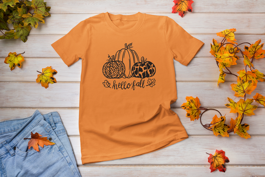 Hello Fall Pumpkin T-Shirt - front view with leaves surrounding and a pair of jeans on a wooden background.