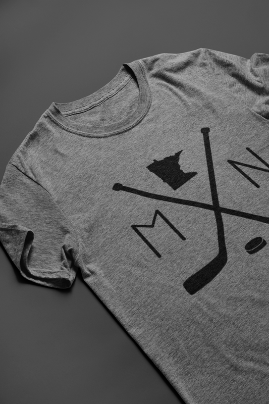 Heather Gray Minnesota Hockey T-Shirt. On the front has a black design with to hockey sticks faced like an X with a puck below in. An M to the left, an N to the right, and an outline of the state of minnesota up top. This is the front view of the shirt laid down "Style view"