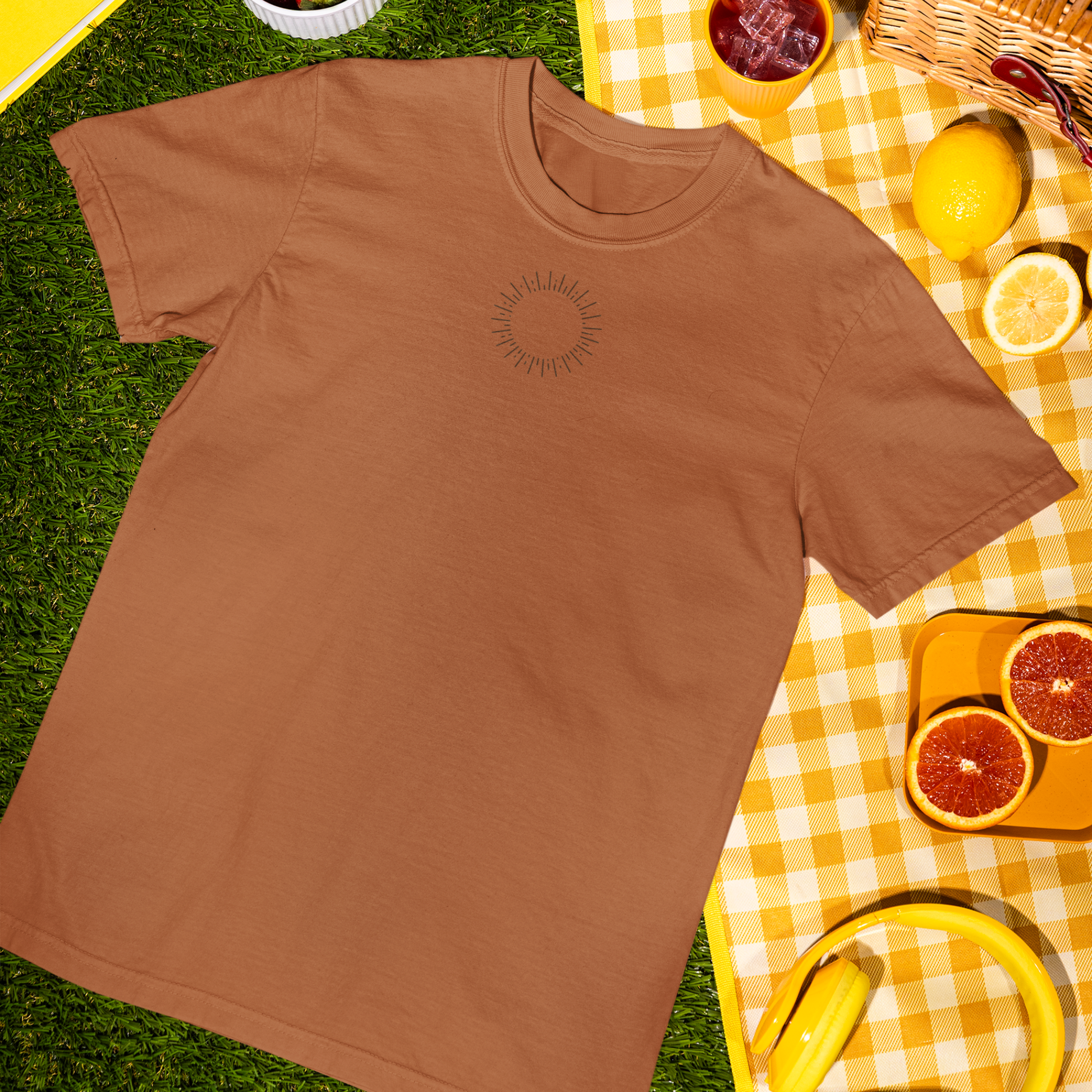 orange sunshine t-shirt on a grassy surface with a yellow checkered tablecloth and picnic items.