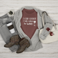 I Can Cook T-Shirt in maroon in a stylized setting featuring a white purse, sunglasses, brown boots, gray jeans & sweater with a coffee cup & plant prop on a wooden bcakground