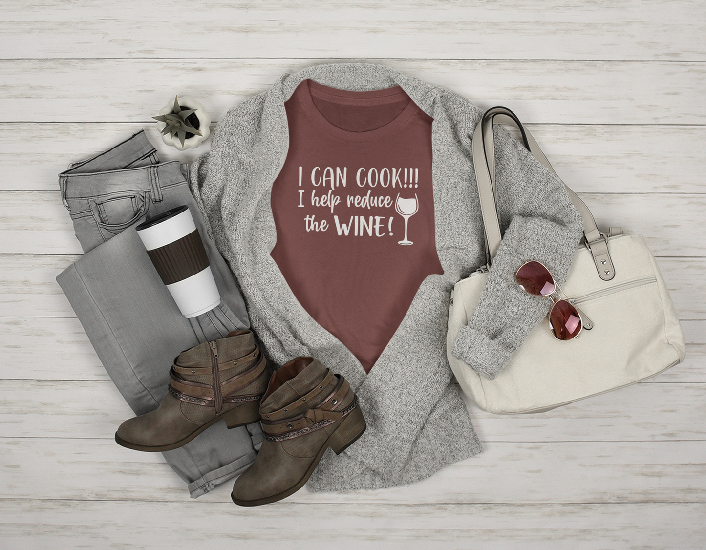 I Can Cook T-Shirt in maroon in a stylized setting featuring a white purse, sunglasses, brown boots, gray jeans & sweater with a coffee cup & plant prop on a wooden bcakground