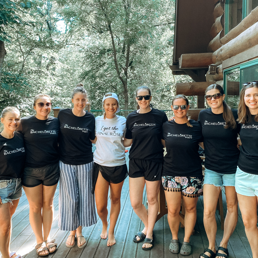 The Bachelorette Party T-Shirt in black. The design in on the front is in white with "The" being smaller script font, "Bachelorette" and "Party" being a bold font. The O in Bachelorette is a diamond ring. This an image of the brides party with the shirts on.