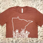 State of Minnesota outline with flowers ranging up the state in white on a heather clay shirt by bella canvas. Front view of the t-shirt on a cute background.