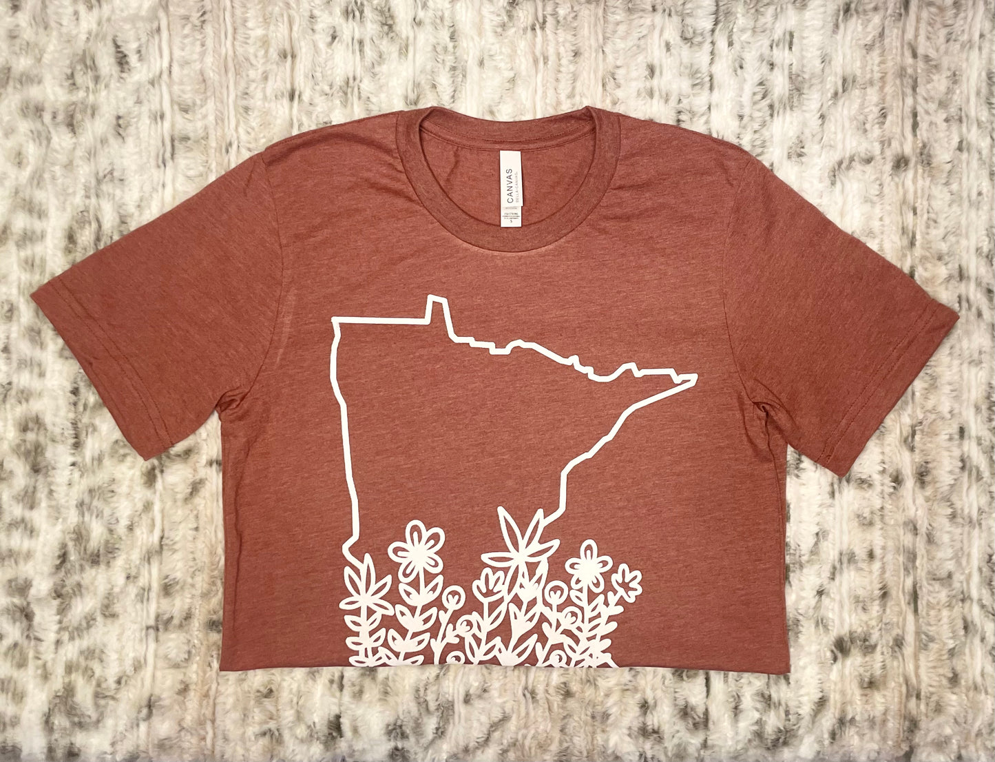 State of Minnesota outline with flowers ranging up the state in white on a heather clay shirt by bella canvas. Front view of the t-shirt on a cute background.