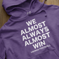 We Almost Always Almost Win Vikings Football Hooded Sweatshirt in purple with white writing. This is the front view of the sweatshirt up close view laying on a hard wood floor.