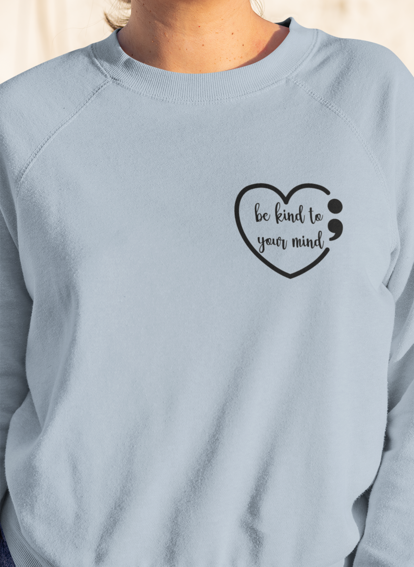 Dear Person Behind Me - Pull Over Sweatshirt in light blue. Designs are in black. The back says "Dear person behind me, the world is a better place with you in it. Love the person in front of you" in a cursive design. The front design is on the right hand side, as a small pocket square with the saying "be kind to your mind" in cursive with a heart and semi colon surrounding it. This is the front view of the sweatshirt on a model (up close view)