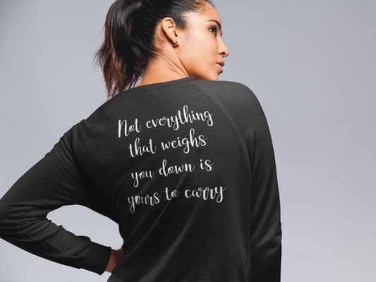 Not Everything That Weighs You Down - Pull Over Sweatshirt in charcoal gray. The back has a white cursive saying of "not everything that weighs you down is yours to carry" with the front corner pocket saying in a cursive font in white of "keep smiling". This is the back view of the sweatshirt on a model posing