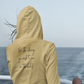 Be The Change Hooded Sweatshirt in a light yellow. The back has a black cursive writing saying "be the change you wish to see in the world." The front has a small flower with stem in black - pocket style. This is the back view of the sweatshirt on a model on the back of a boat with her hood up looking out at the water, and her hair waving in the wind.