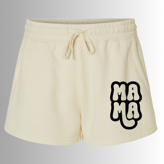 Mama Shorts in cream with a comfy warm fabric. Draw strings loop the front and small emblem of "mama" is on the right hand side of the short in black - on the front. This is the front view of the shorts with a gradient white to gray background.