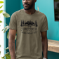 The Breweries Are Calling And I Must Go - T-Shirt in a heather Olive Garden. Black Design on the front with the saying "the breweries are calling and I must go" with arrows pointing at "are calling" hoops surrounding the "breweries" and pine trees, mountains and 2 black bears above the saying. This is the front view of the shirt on a male model hanging out in a brewery setting.