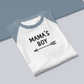 Mama's Boy - Three Quarter Baseball T-Shirt. Sleeves in a Heather light blue on the sleeves with a white base. Mama's Boy is in black with an arrow below it pointing to the left. This is the front view of the shirt - folded on a blue and gray background.