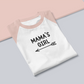Mama's Girl - Three Quarter Sleeve T-Shirt. Sleeves are heather peach and base is white with the Mama's Girl writing in black with a cute arrow pointing to the left underneath. This is a photo of the front of the shirt folded on a pink and gray base.