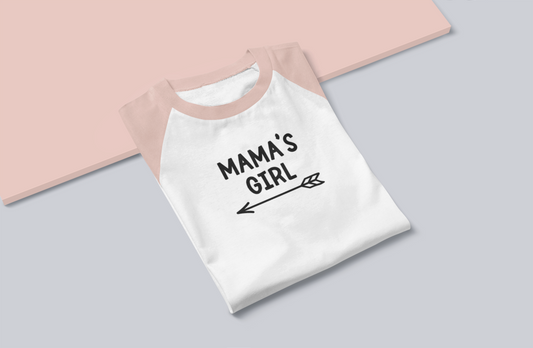 Mama's Girl - Three Quarter Sleeve T-Shirt. Sleeves are heather peach and base is white with the Mama's Girl writing in black with a cute arrow pointing to the left underneath. This is a photo of the front of the shirt folded on a pink and gray base.