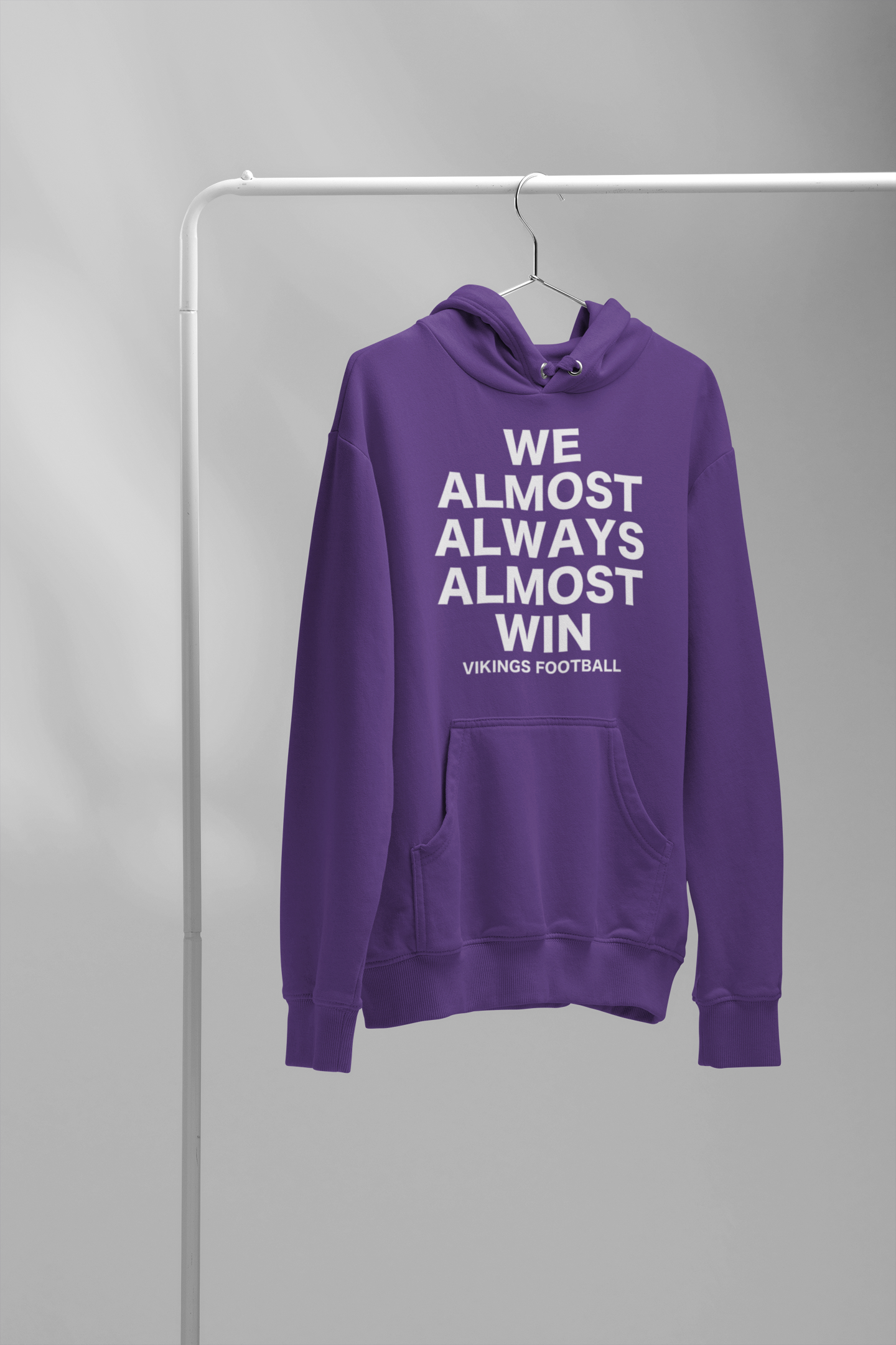 We Almost Always Almost Win Vikings Football Hooded Sweatshirt in purple with white writing. This is the front view of the sweatshirt on a wired hanger hanging on a clothing rack.