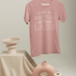 Life Is Better By The Lake - T-Shirt in Mauve with white writing hanging on a hanger and someone holding said hanger. Styled items below the item on a staircase like set.
