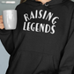 Raising Legends Black Sweatshirt Hoodie - Front ViewRaising Legends - Hooded Sweatshirt in black with white writing. Raising is curve at the top and legends is straight on the bottom. Features an innovative print process that raises the ink for a more defined design. This is the front view of the sweatshirt on a model holding a cup of coffee and posing.