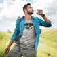 Woodsy Bear Silhouette - T-Shirt in gray with black design on a male model out in a field with a chambray denim shirt and olive green pants with a backpack hanging on his shoulder sipping water out of a water bottle.