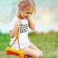 Cutest Clover In The Patch T-Shirt for youth and toddler in white. Adorable saying in green with twinkles and 4 leaf clovers. This is the front view of the shirt on a cute little girl swinging on a swing and smiling.