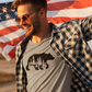 Woodsy Bear Silhouette - T-Shirt in gray with a black bear on it on a male model. The model has a black and white check plaid flannel, with sunglasses carrying an American flag behind his back.