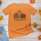 Hello Fall Pumpkin T-Shirt - front view with leaves surrounding and a pair of jeans on a wooden background.