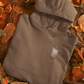 Brown hoodie with a coffee cup design on a bed of autumn leaves