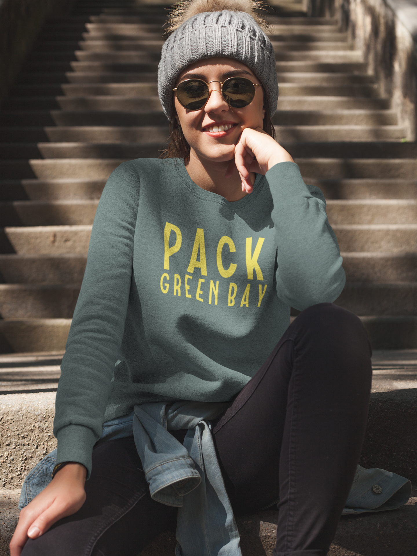 Green Bay Packers Crewneck Sweatshirt - front view on a female model sitting on stairs posing with a jean jacket wrapped around her waist, a hat and sunglasses on.