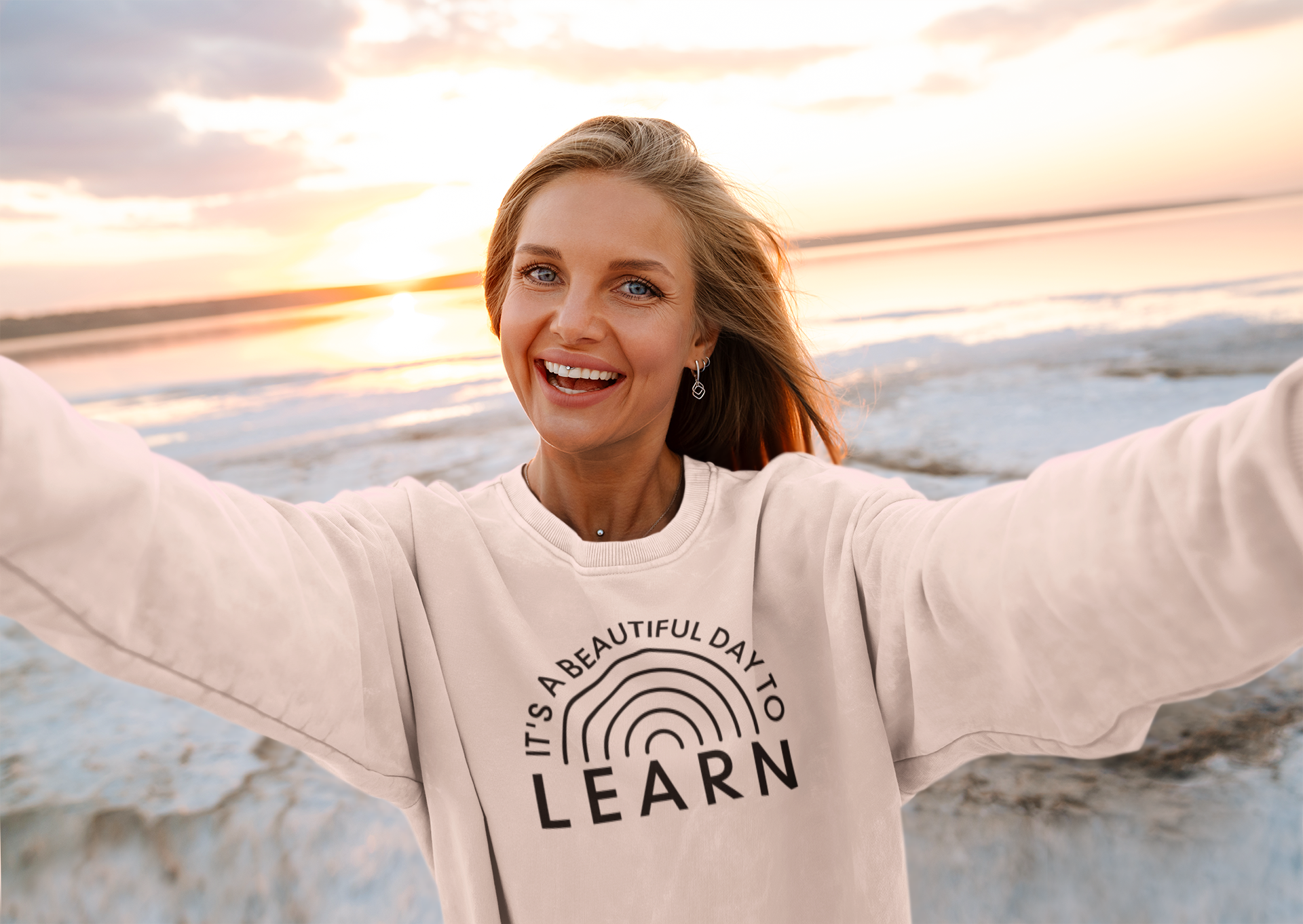 It's A Beautiful Day To Learn Crewneck Sweatshirt in pink on a female model on a female model with a sunset behind her and an ocean view.