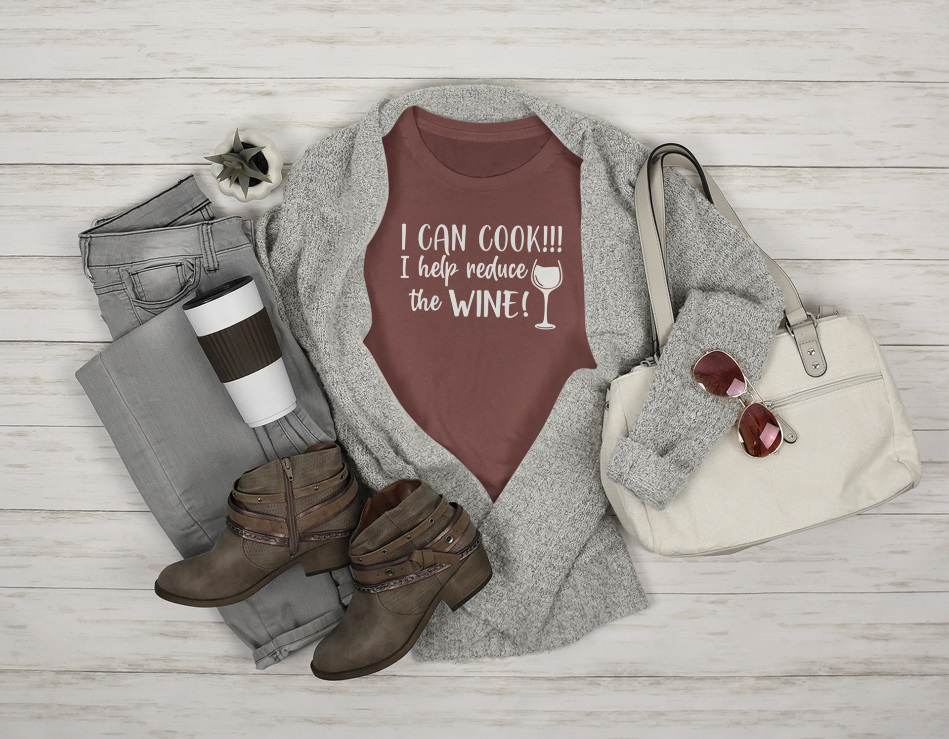 I Can Cook T-Shirt in maroon in a stylized setting featuring a white purse, sunglasses, brown boots, gray jeans & sweater with a coffee cup & plant prop on a wooden bcakground