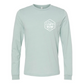 Life is Better at the Lake - Long Sleeve T-Shirt (front view) with patch on front that says Lake BumLife is Better at the Lake - Long Sleeve T-Shirt in heather dusty blue. The back of the shirt has a white design with the saying "Life is better at the lake" with lake waves, pine trees, and a loon all squared into a frame. The front has the saying "lake bum" with a lake wave and sun all boxed into a hexagon on the small square pocket (right). This is the front view of the shirt.