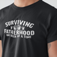 Surviving Fatherhood One Beer At A Time - Black T-Shirt - front view in white writing. Between the word surviving and fatherhood is different glasses of beer mugs. This is the front view of the shirt up close on a model.