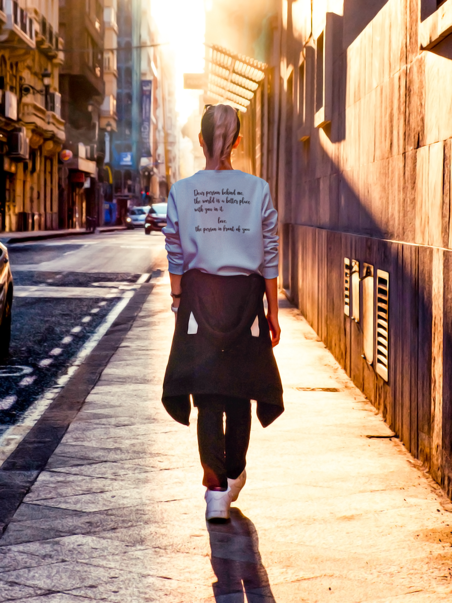 Dear Person Behind Me - Pull Over Sweatshirt in light blue. Designs are in black. The back says "Dear person behind me, the world is a better place with you in it. Love the person in front of you" in a cursive design. The front design is on the right hand side, as a small pocket square with the saying "be kind to your mind" in cursive with a heart and semi colon surrounding it. This is the back view of the sweatshirt on a model walking down a city street.