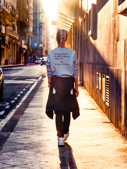Dear Person Behind Me - Pull Over Sweatshirt in light blue. Designs are in black. The back says "Dear person behind me, the world is a better place with you in it. Love the person in front of you" in a cursive design. The front design is on the right hand side, as a small pocket square with the saying "be kind to your mind" in cursive with a heart and semi colon surrounding it. This is the back view of the sweatshirt on a model walking down a city street.