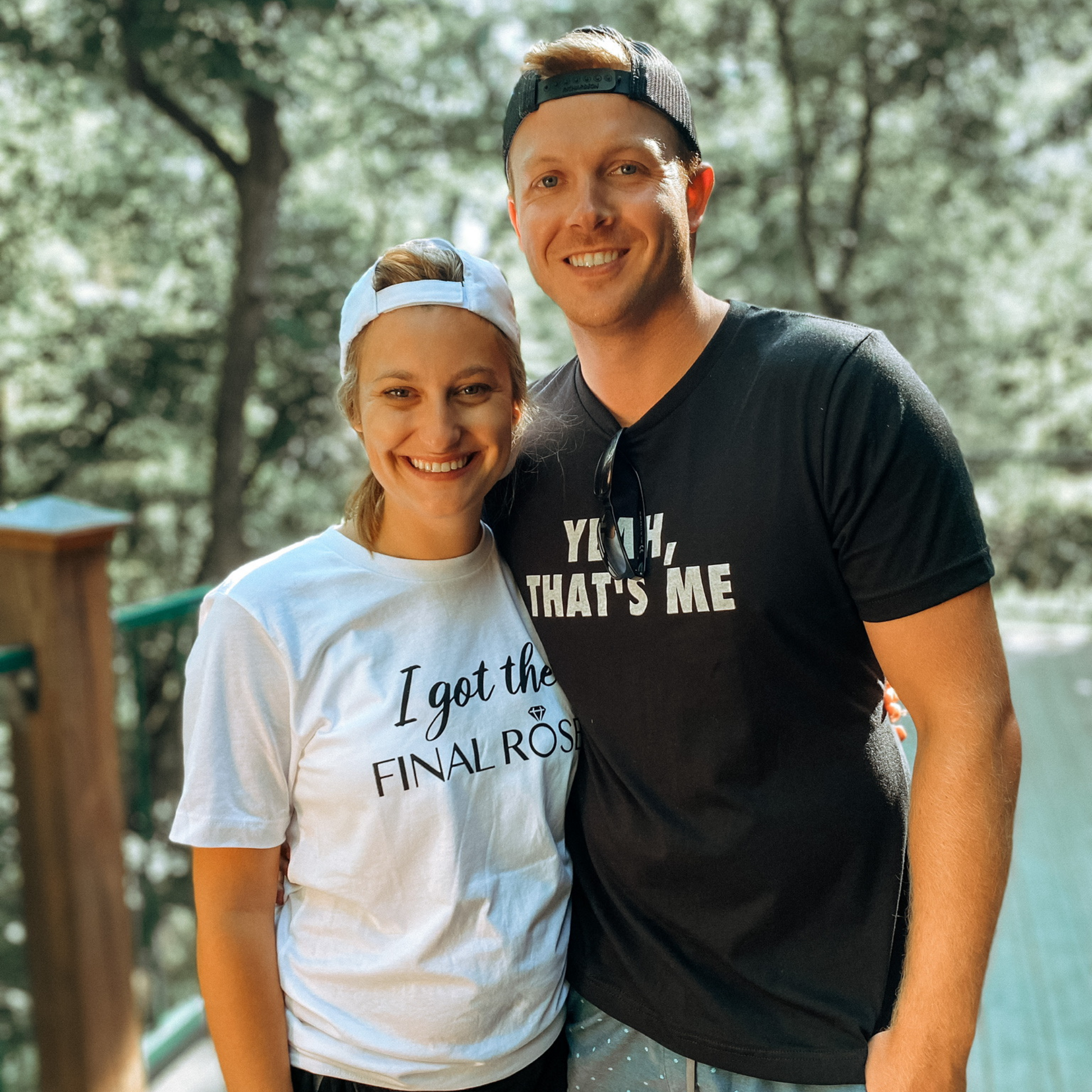 I Got The Final Rose Bride T-Shirt in white. The front has the saying "I got the final rose" with the O in rose being a diamond ring. The "I got the" is in a script font with the "final rose" is in a bold font. Design is in black. This is an image of a bride wearing the t-shirt with her future mr.