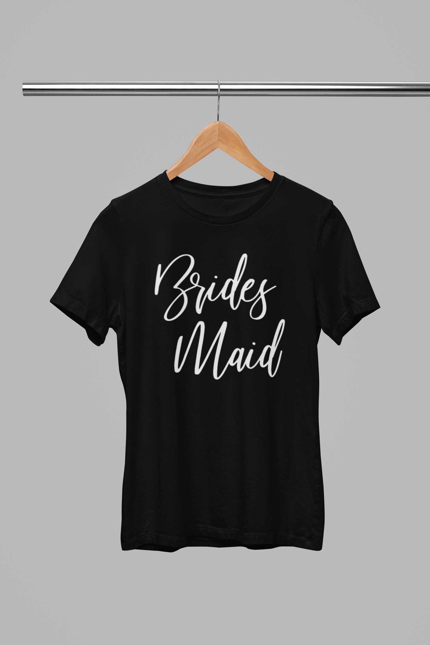 Bridesmaid T-Shirt in black with a white script font writing on the front of the tee. This is the front view of the t-shirt hanging on a wooden hanger hanging on a silver metal clothing rack