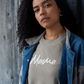 Green Mama - Pull Over Sweatshirt - front viewMama - Pull Over Sweatshirt in olive green with a white cursive modern font design with "mama" on it. This is the front view of the sweatshirt on a female model leaned up against a wooden background with a serious face looking at the camera. She has the Mama sweatshirt on with a gray fleece and jean jacket over the top of it.